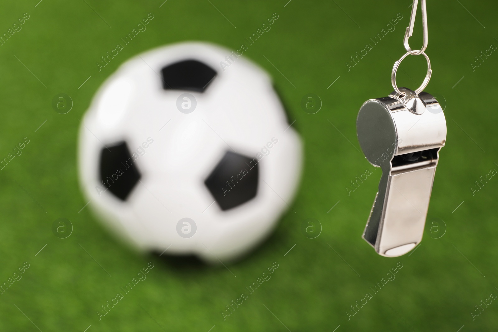 Photo of Football referee equipment. Metal whistle and soccer ball on green grass, closeup with space for text