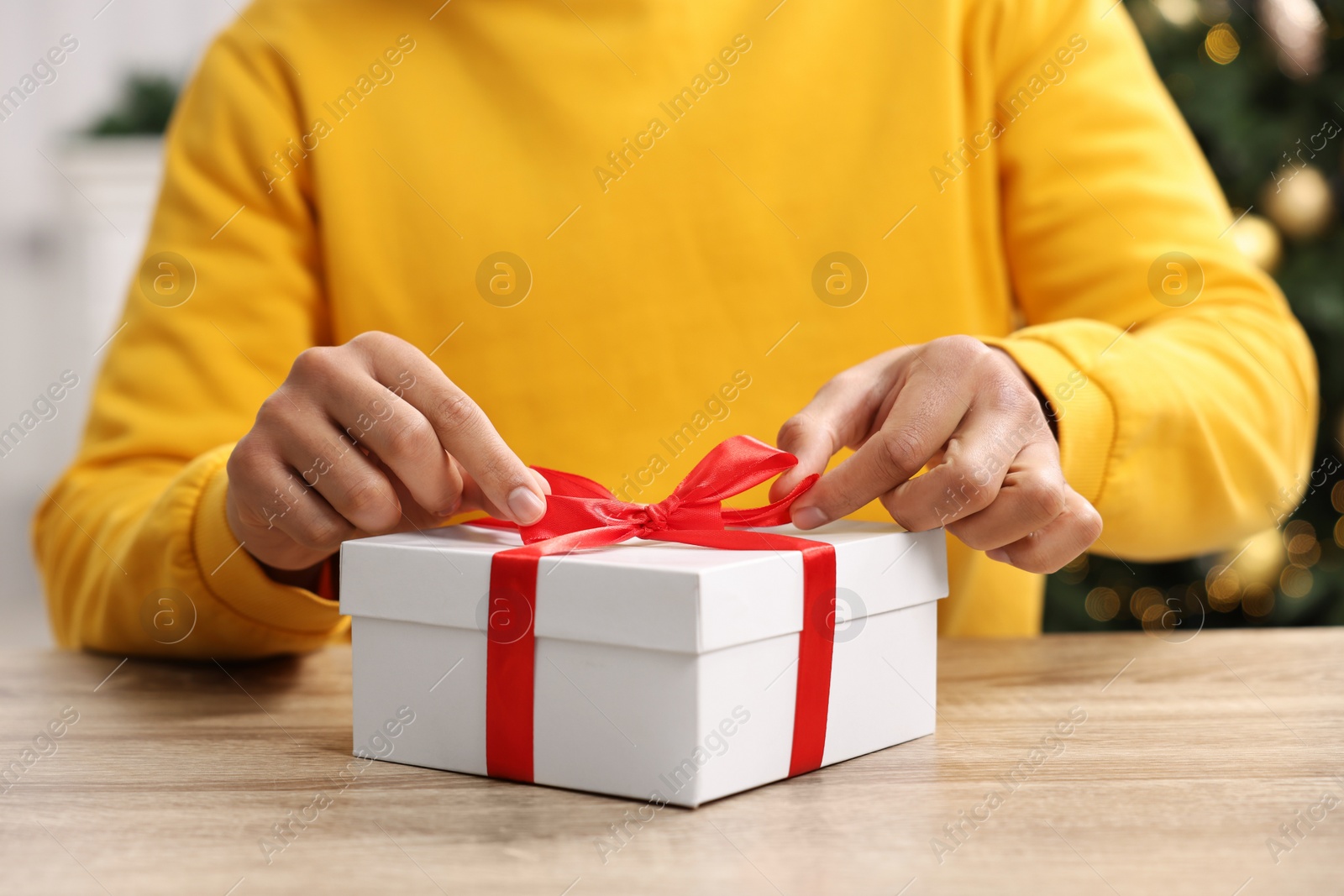 Photo of Man opening Christmas gift at wooden table indoors, closeup