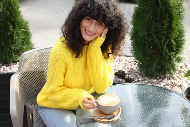 Photo of Young woman in stylish yellow sweater with cup of coffee at table outdoors