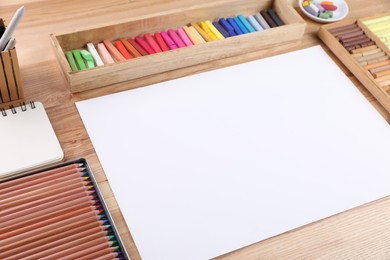 Photo of Blank paper, soft pastels and drawing pencils on wooden table at artist's workplace. Space for design