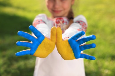 Photo of Little girl with hands painted in Ukrainian flag colors outdoors, closeup. Love Ukraine concept