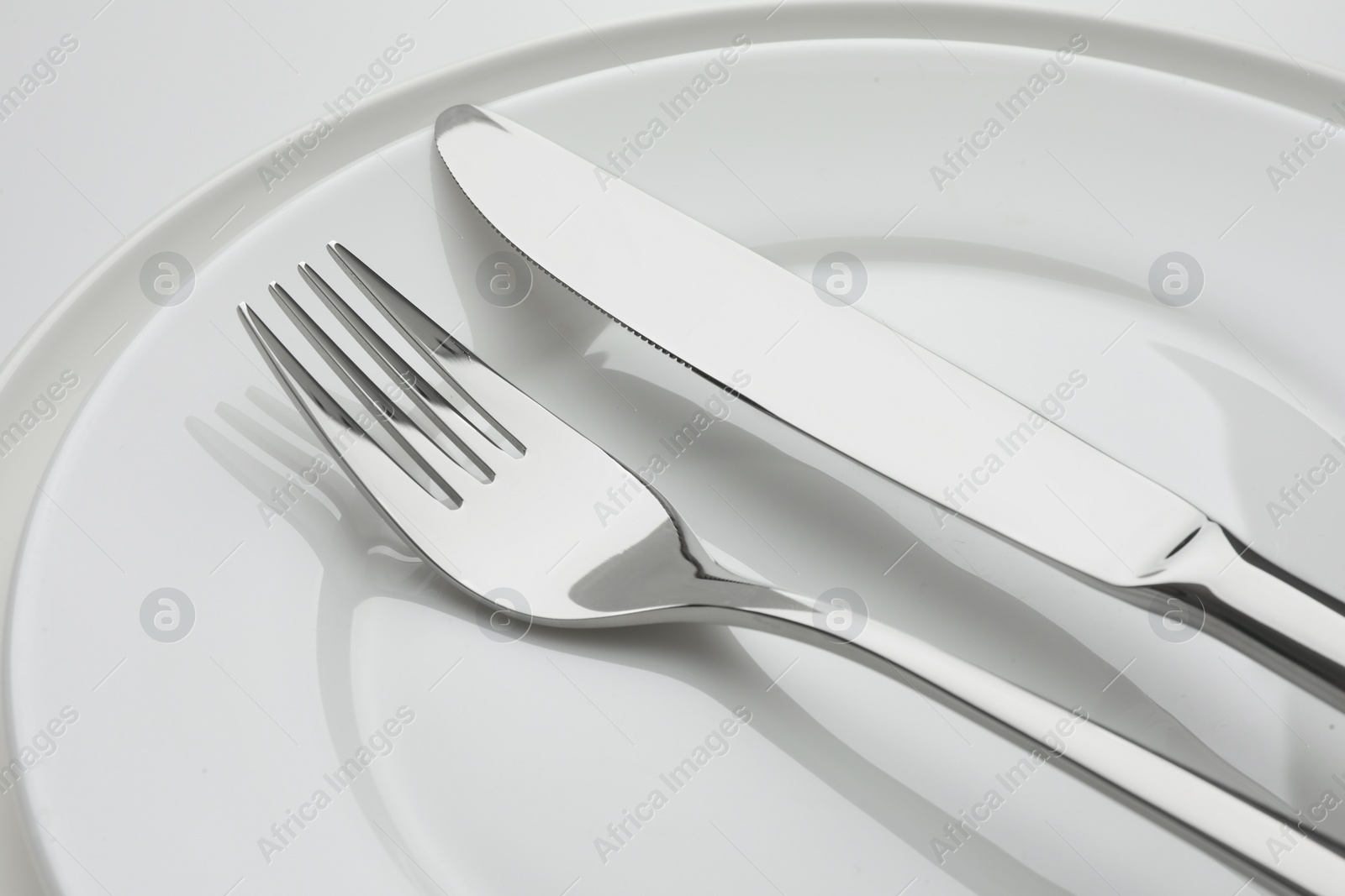Photo of Clean plates, fork and knife on white background, closeup