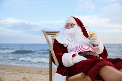 Photo of Santa Claus with cocktail relaxing on beach, space for text. Christmas vacation