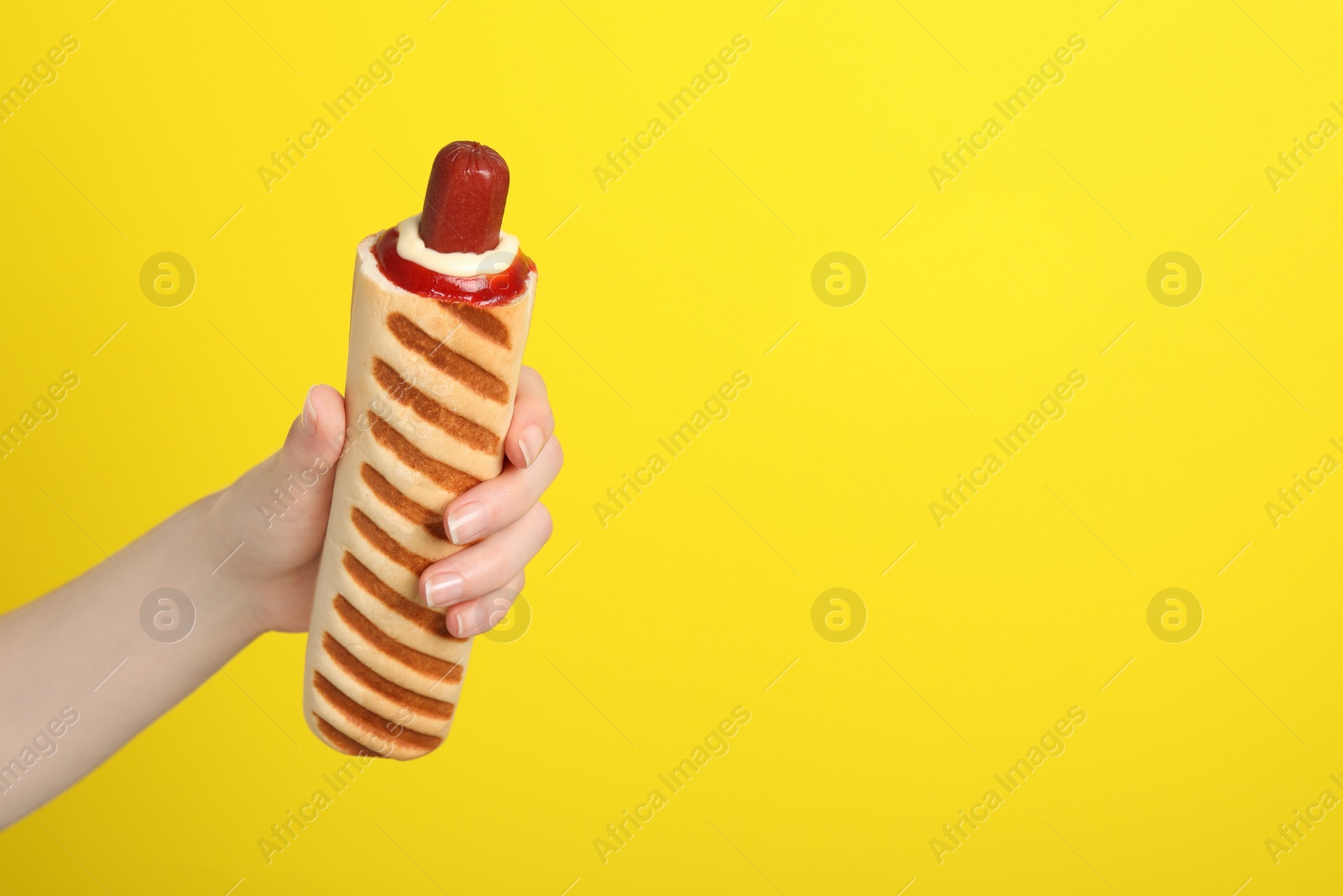 Photo of Woman holding delicious french hot dog on yellow background, closeup. Space for text