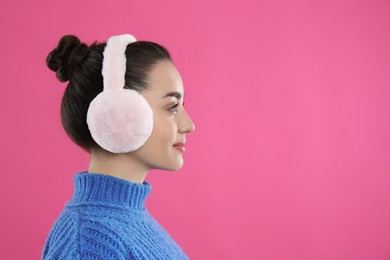 Photo of Beautiful young woman wearing earmuffs on pink background. Space for text