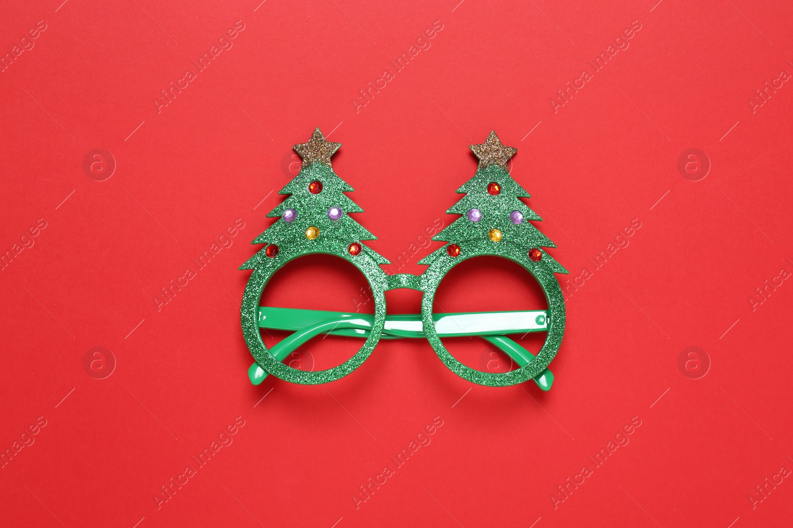 Photo of Funny glasses in shape of Christmas tree on red background, top view