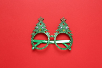 Photo of Funny glasses in shape of Christmas tree on red background, top view