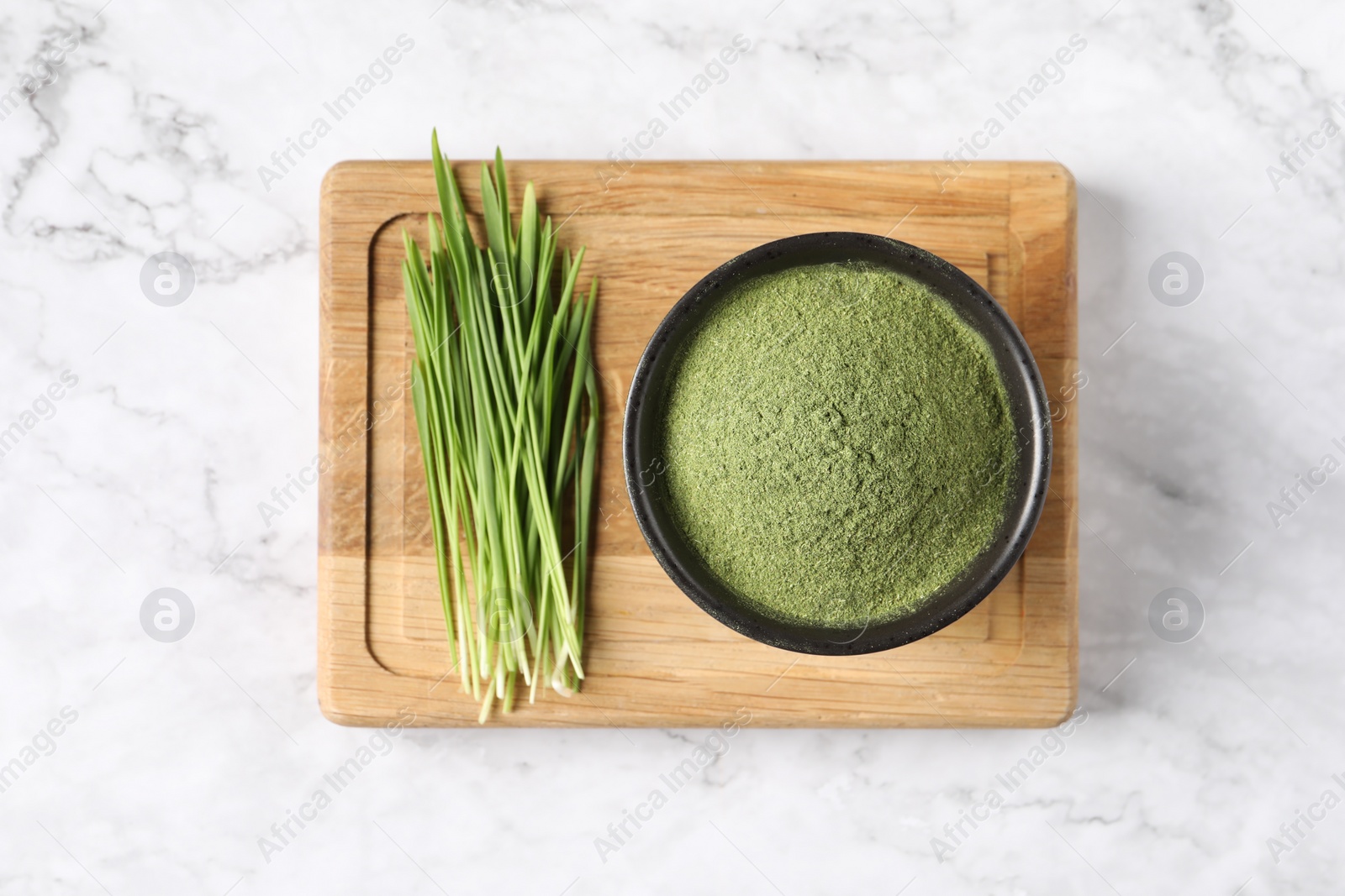 Photo of Wheat grass powder in bowl and fresh sprouts on white marble table, top view