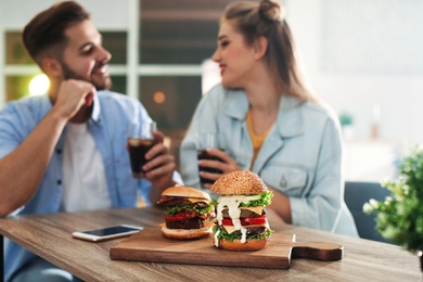 Photo of Young couple having lunch in restaurant, focus on board with burgers