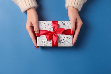 Photo of Christmas present. Woman with gift box on blue background, top view