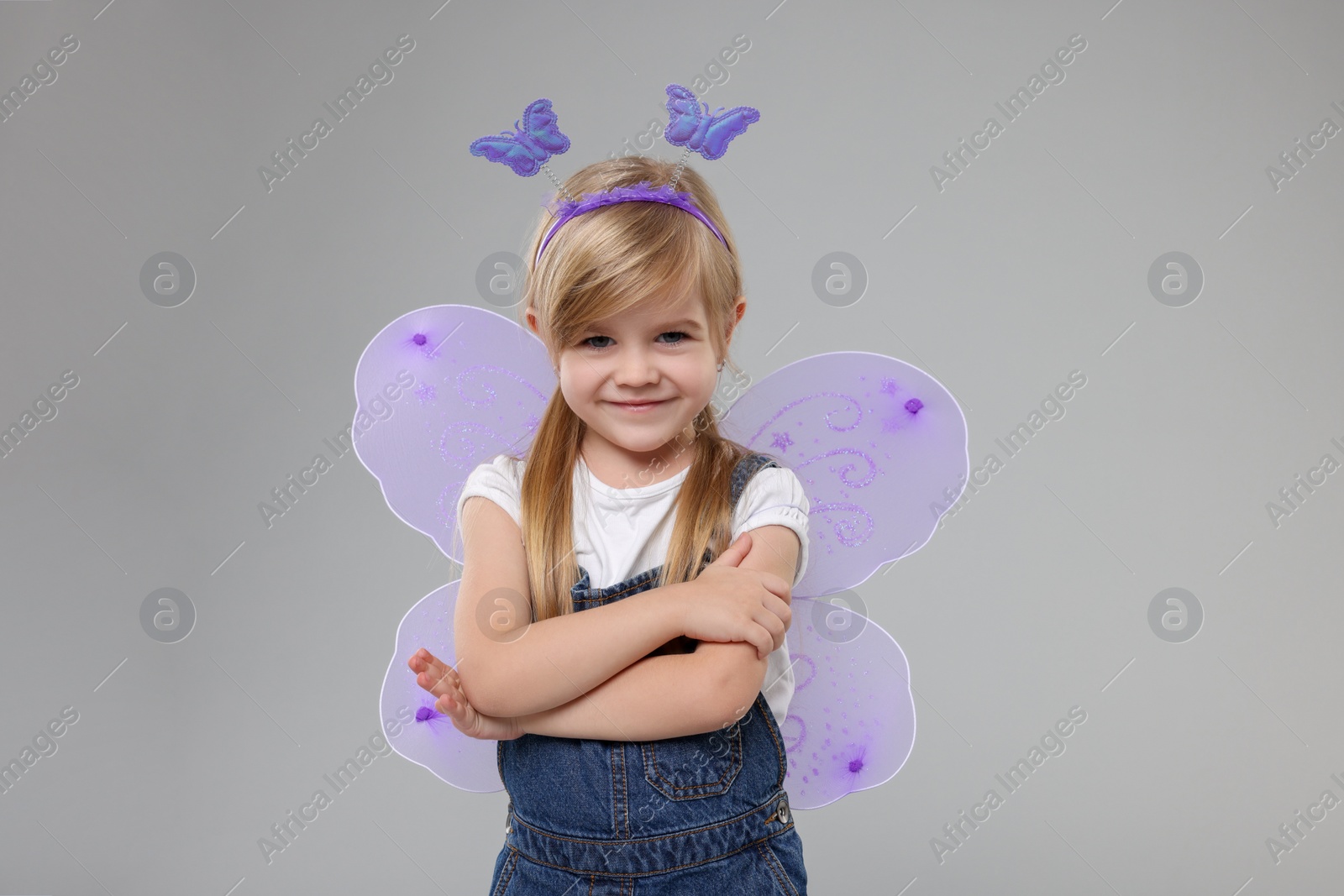 Photo of Cute little girl in fairy costume with violet wings on light grey background