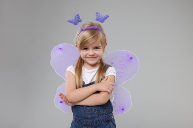 Photo of Cute little girl in fairy costume with violet wings on light grey background