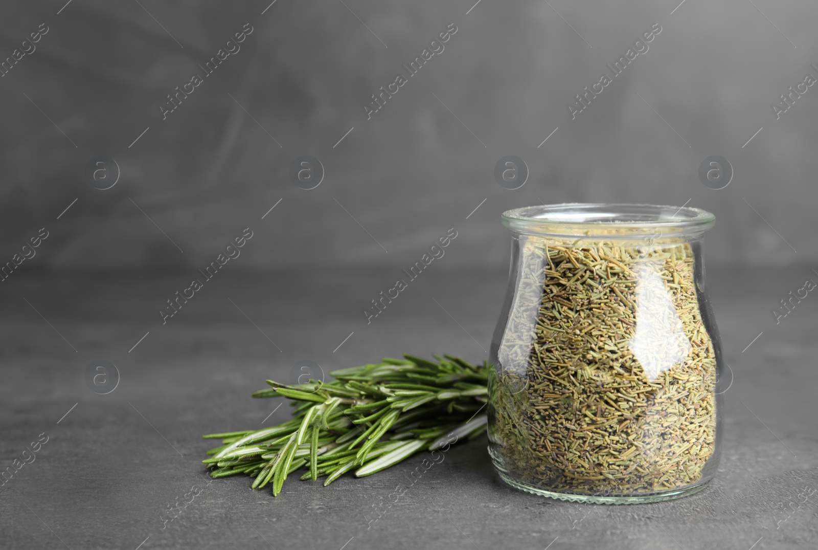 Photo of Jar of dried rosemary and fresh bunch on grey table, space for text