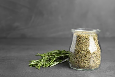 Photo of Jar of dried rosemary and fresh bunch on grey table, space for text