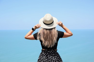 Photo of Woman with hat near sea on sunny day, back view