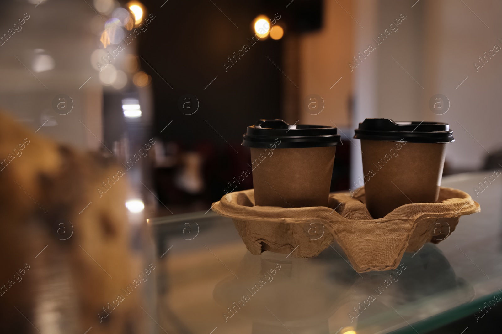 Photo of Takeaway coffee cups with cardboard holder on glass table in cafe