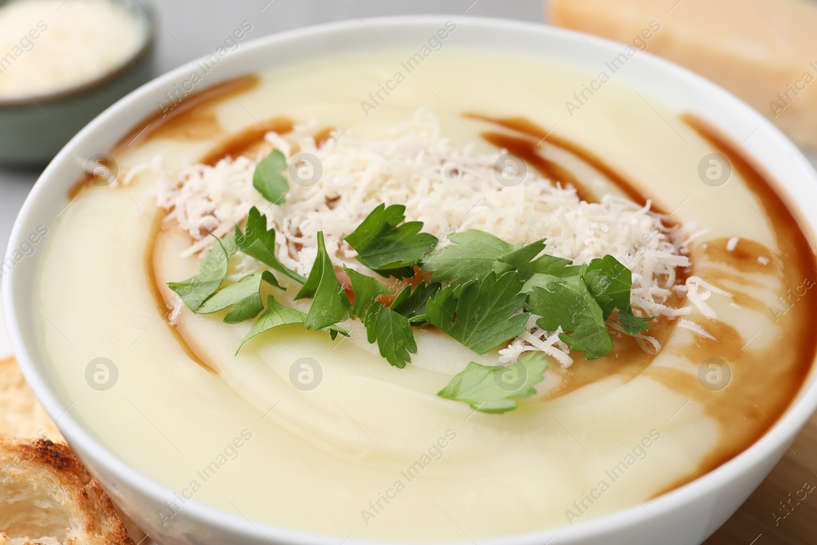 Photo of Delicious cream soup with parmesan cheese, soy sauce and parsley in bowl, closeup