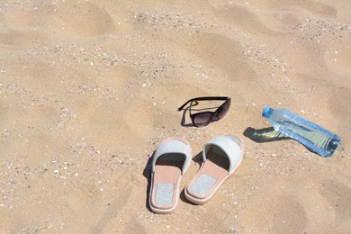Photo of Stylish sunglasses, slippers and bottle of water on sand, space for text. Beach accessories