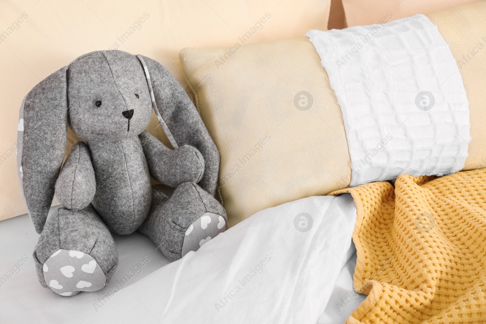 Photo of Cute toy rabbit on bed in child's room interior. Space for text