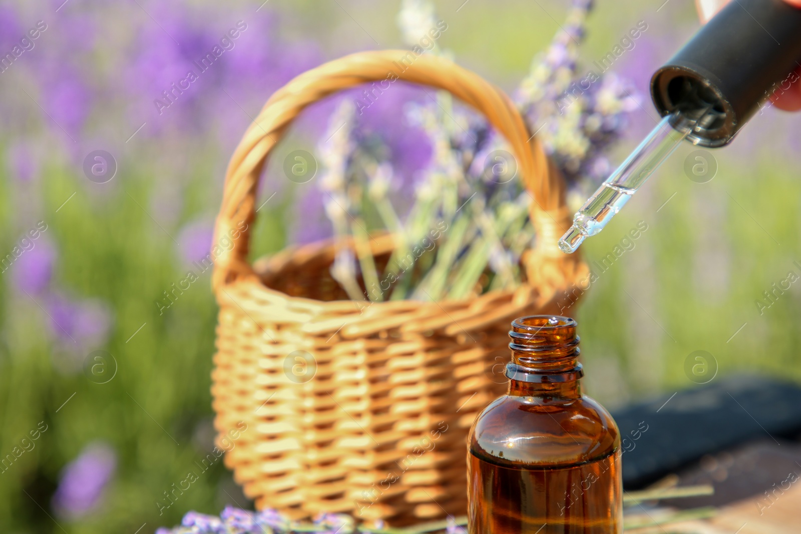 Photo of Dripping essential oil from pipette into bottle near lavender on wooden table outdoors, closeup. Space for text