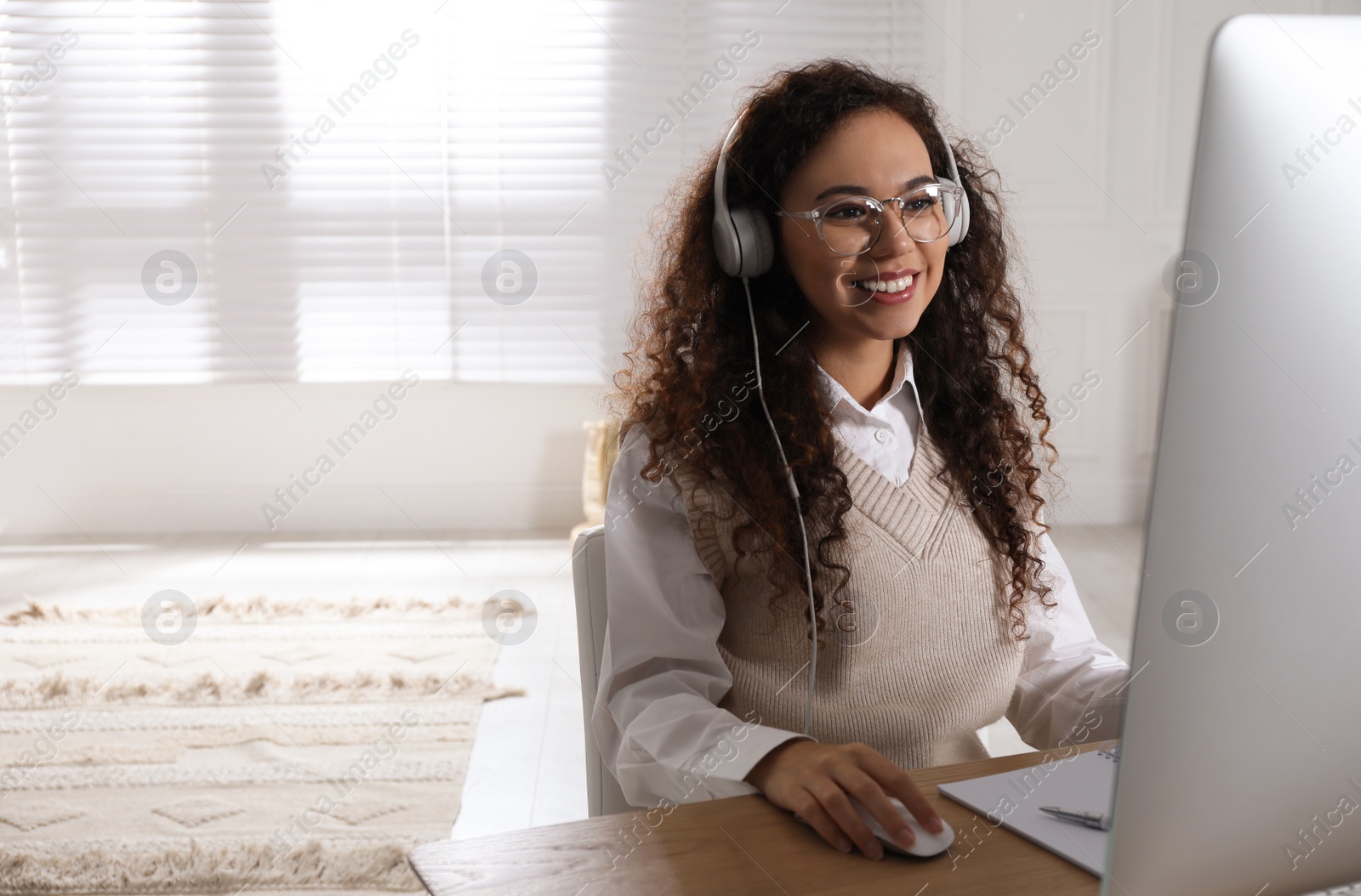 Photo of African American woman with headphones using modern computer for studying at home. Distance learning