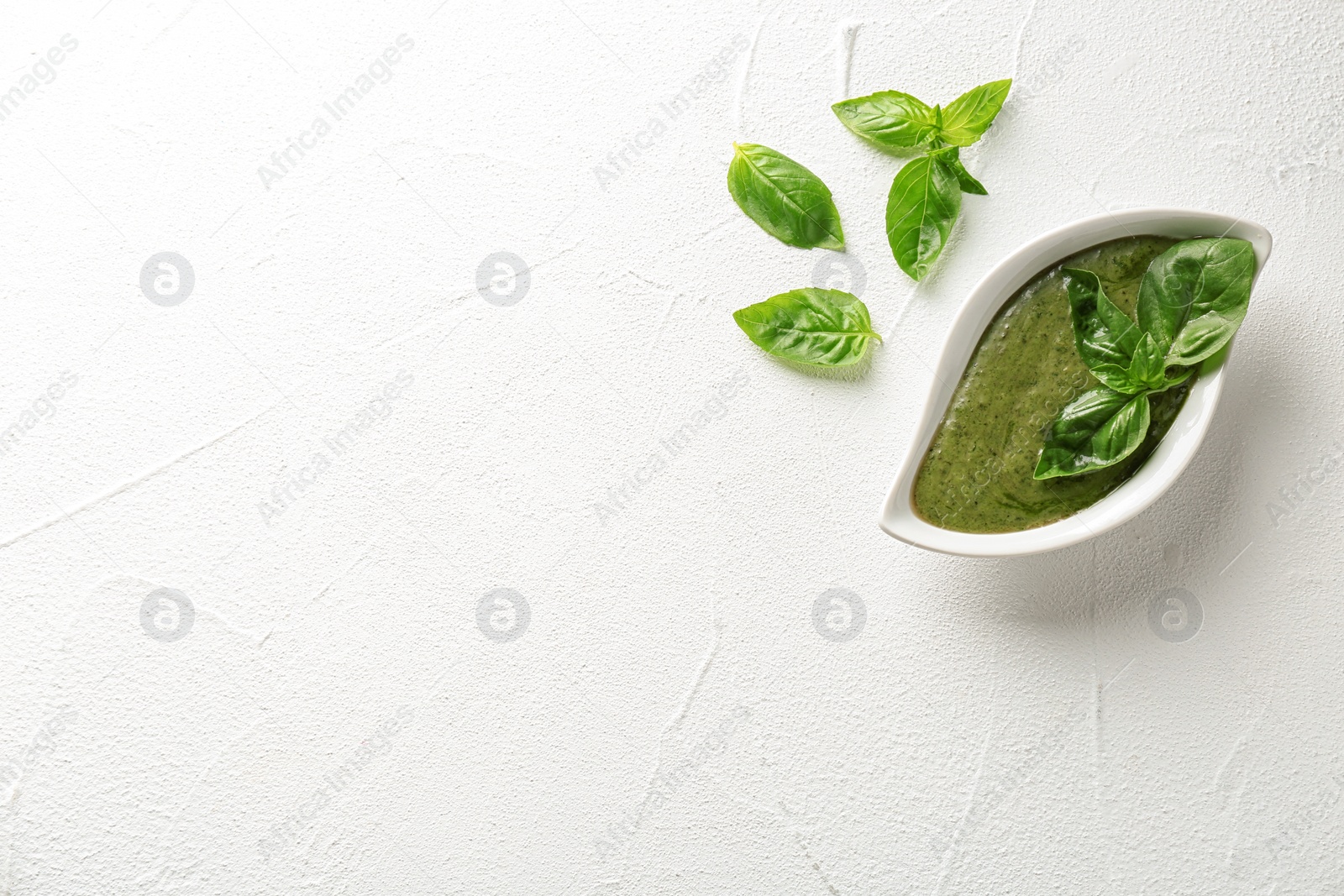 Photo of Sauce in gravy boat and basil leaves on white table, top view with space for text