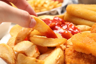 Photo of Woman taking delicious baked potato wedge with ketchup at table, closeup