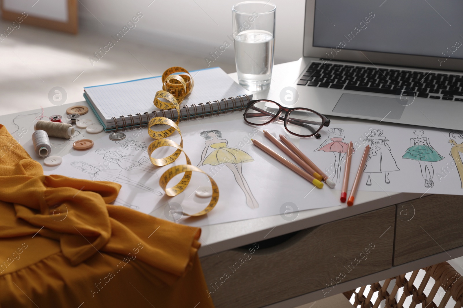 Photo of Sketches of clothes and different stuff on white table indoors. Fashion designer's workplace