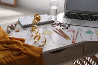 Sketches of clothes and different stuff on white table indoors. Fashion designer's workplace