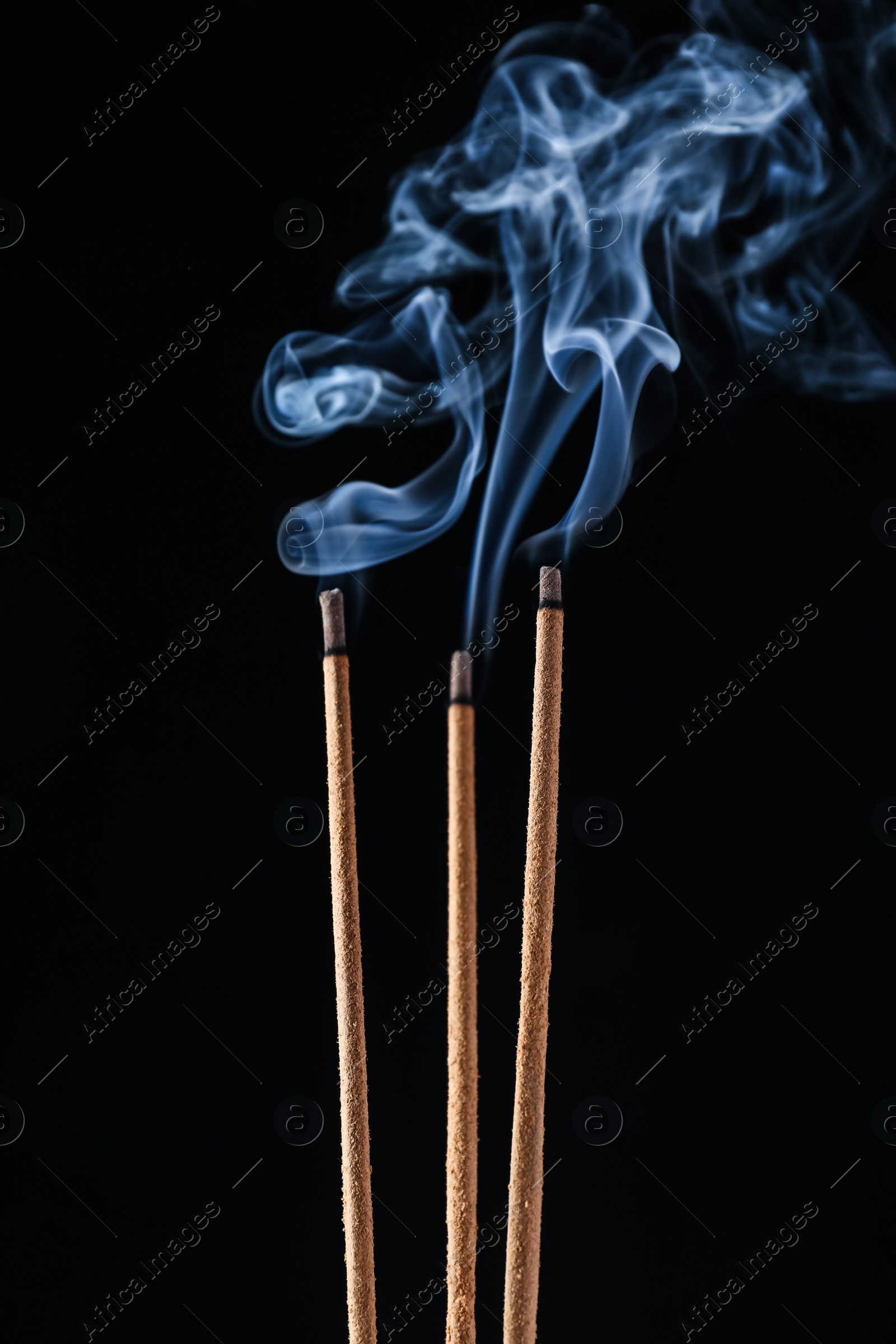 Photo of Incense sticks smoldering on black background, closeup