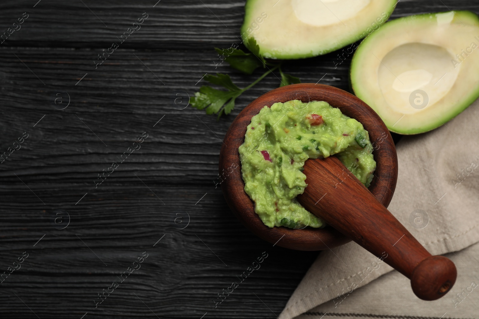 Photo of Mortar with delicious guacamole and ingredients on black wooden table, flat lay. Space for text