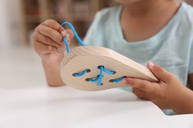 Motor skills development. Little girl playing with wooden lacing toy at table indoors, closeup