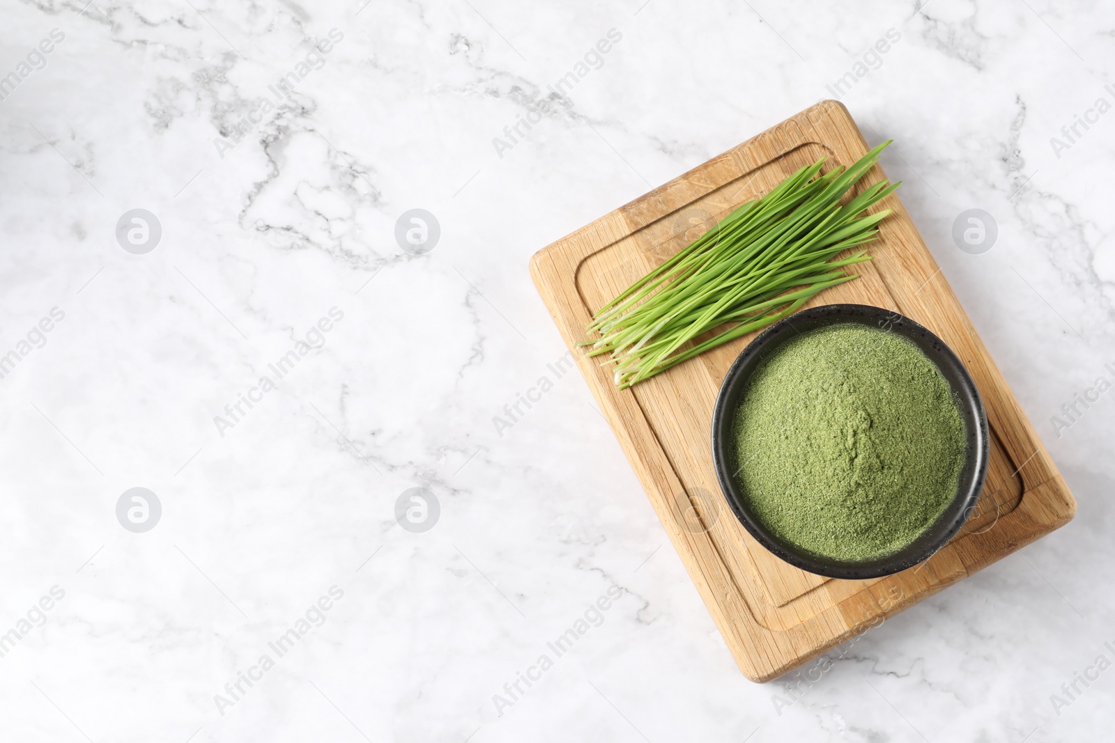 Photo of Wheat grass powder in bowl and fresh sprouts on white marble table, top view. Space for text