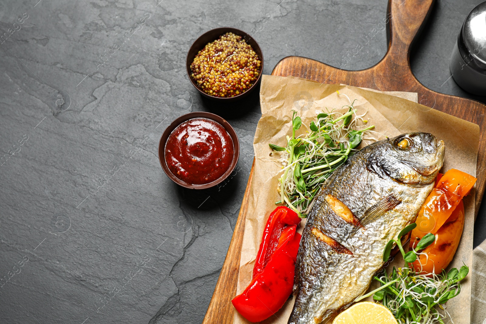 Photo of Delicious roasted fish and vegetables on dark grey table, flat lay