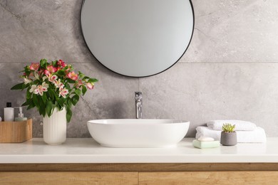 Vase with beautiful Alstroemeria flowers and toiletries near sink in bathroom