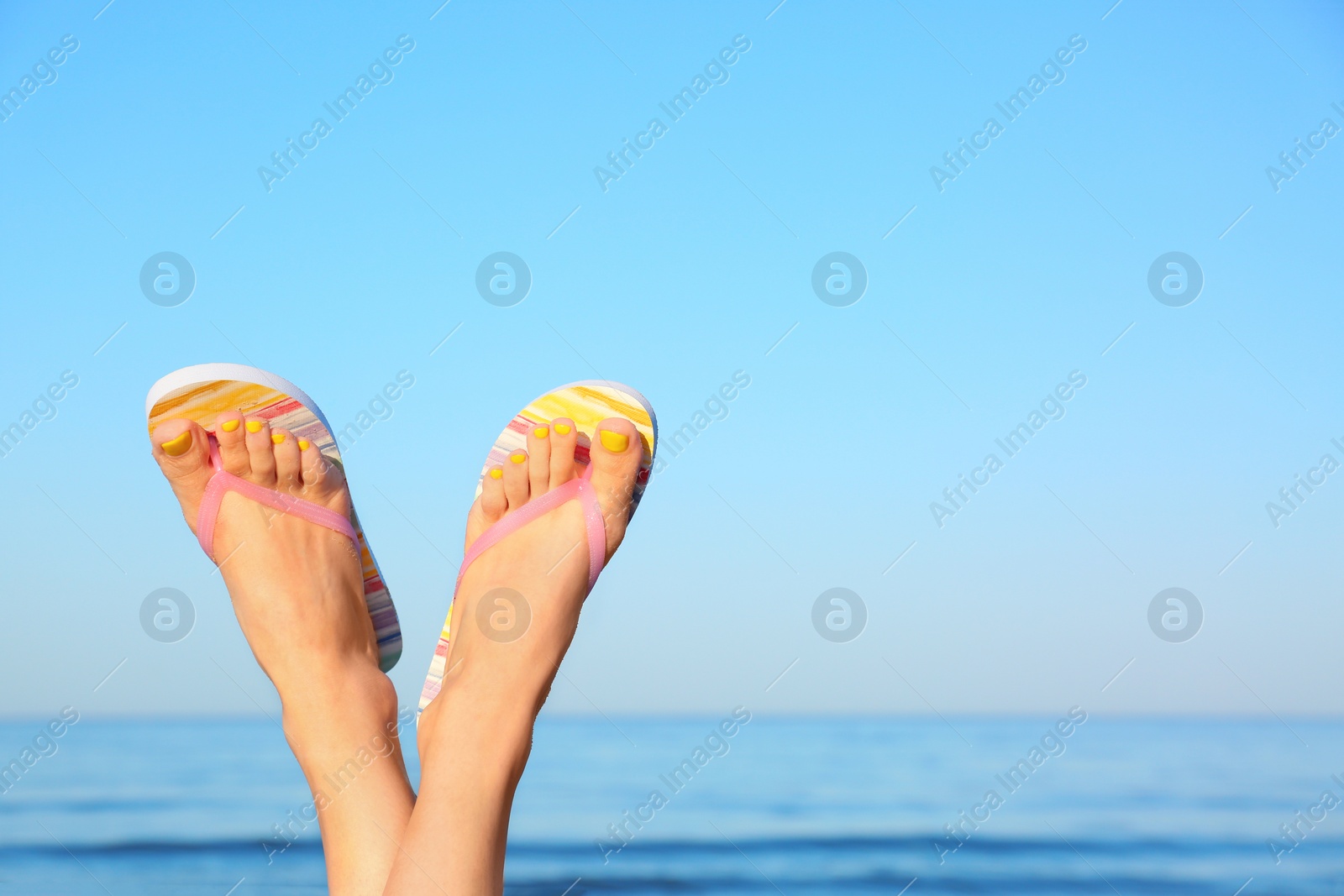 Photo of Closeup of woman wearing flip flops near sea, space for text. Beach accessories