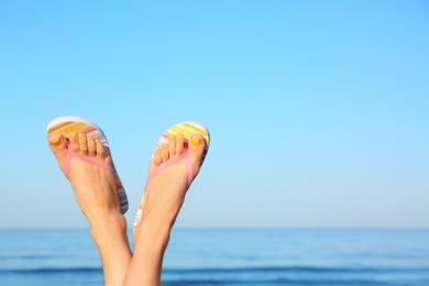 Photo of Closeup of woman wearing flip flops near sea, space for text. Beach accessories