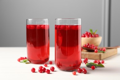 Tasty cranberry juice in glasses and fresh berries on white wooden table, closeup