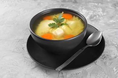 Photo of Tasty chicken soup with noodles, carrot and parsley in bowl served on light textured table, closeup