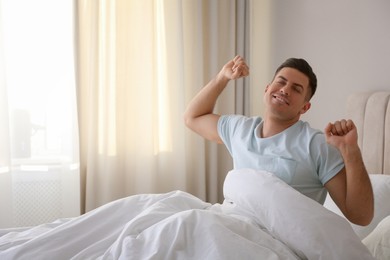 Man stretching on bed with white linens at home. Space for text