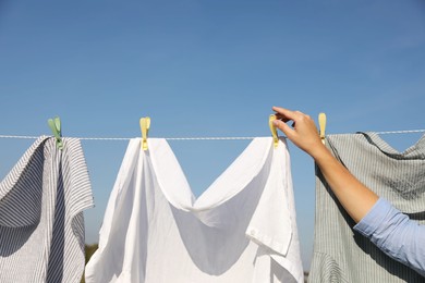 Photo of Woman hanging clothes with clothespins on washing line for drying against blue sky outdoors, closeup