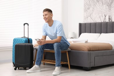 Photo of Smiling guest with smartphone and suitcase in stylish hotel room