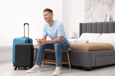 Smiling guest with smartphone and suitcase in stylish hotel room