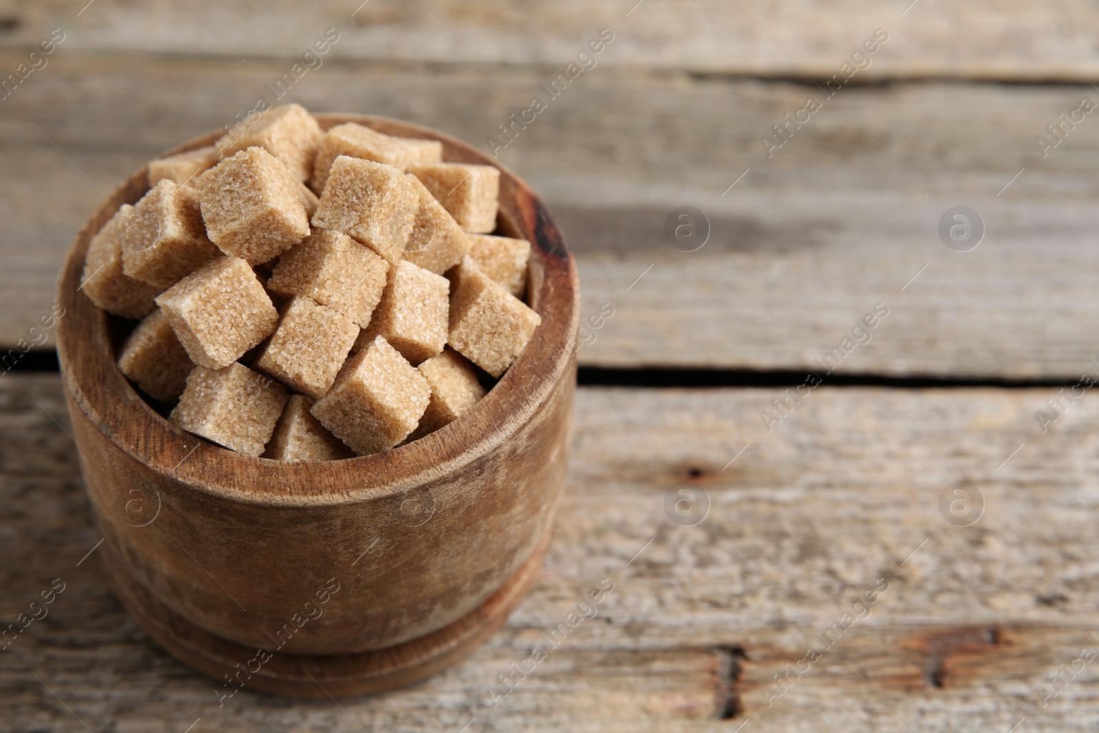 Photo of Bowl with brown sugar cubes on wooden table, closeup. Space for text