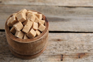 Photo of Bowl with brown sugar cubes on wooden table, closeup. Space for text