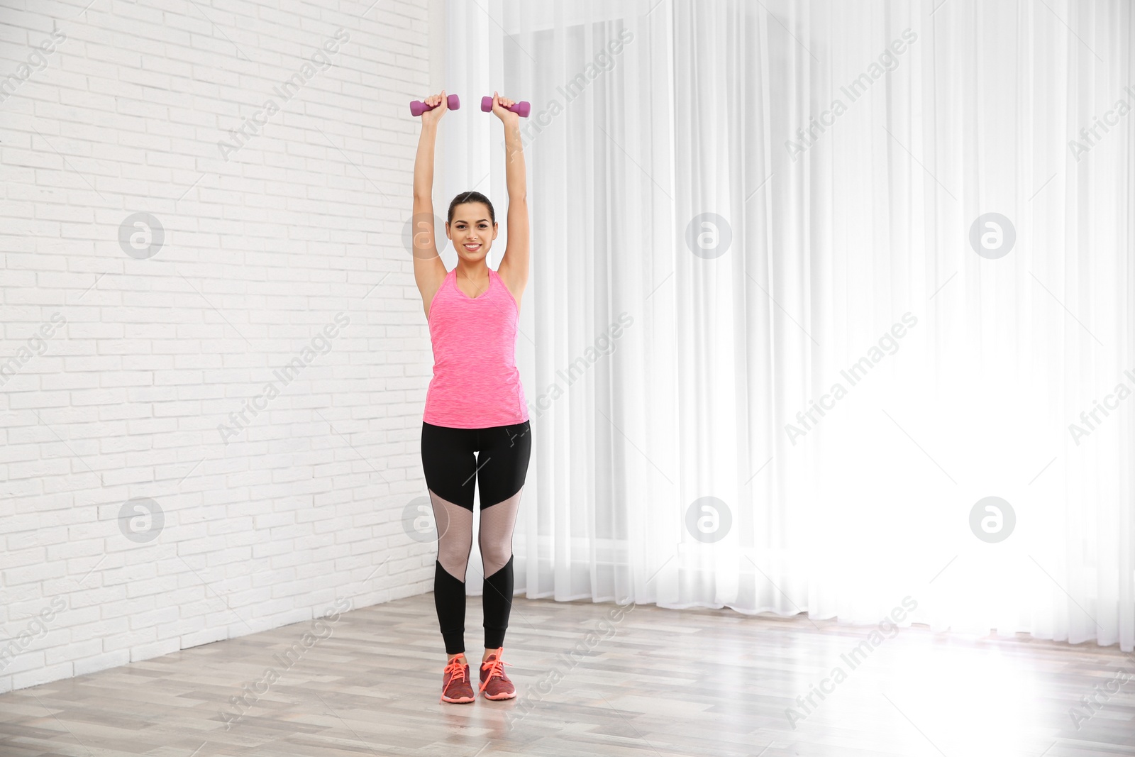 Photo of Young beautiful woman with dumbbells doing exercise at home. Workout and fitness