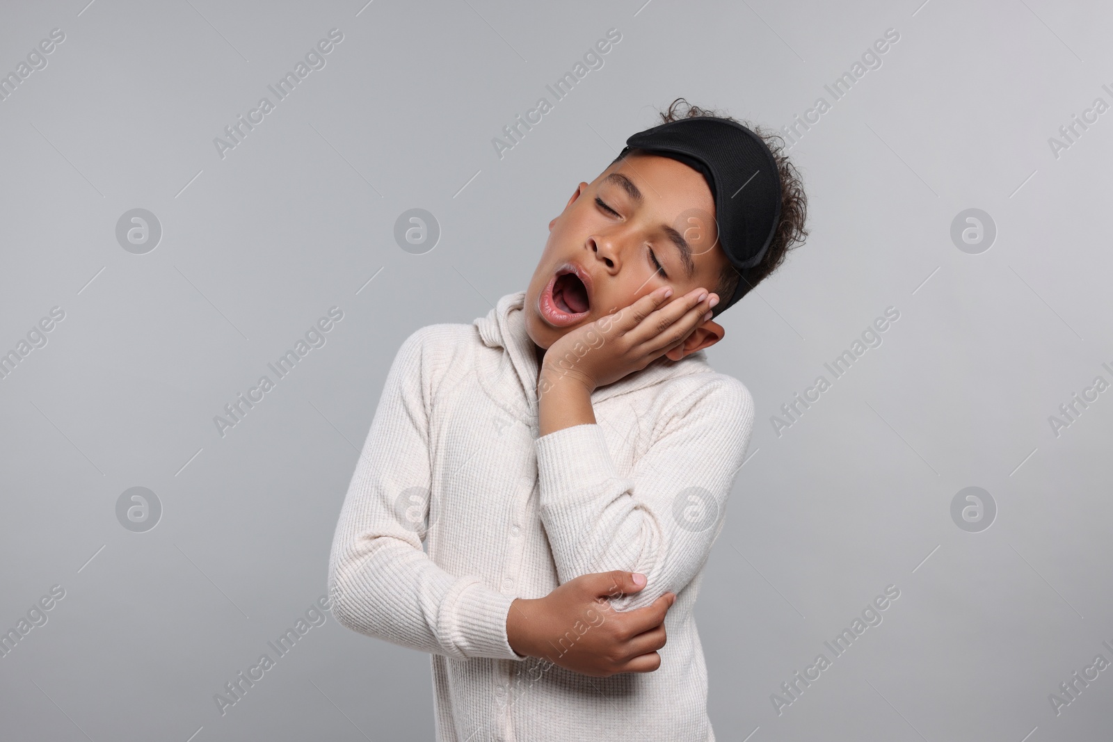 Photo of Boy with sleep mask yawning on grey background. Insomnia problem