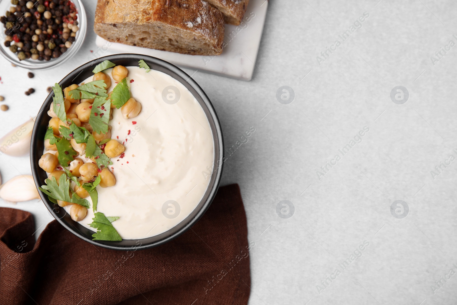 Photo of Flat lay composition of tasty chickpea soup in bowl, bread and spices served on light grey table. Space for text