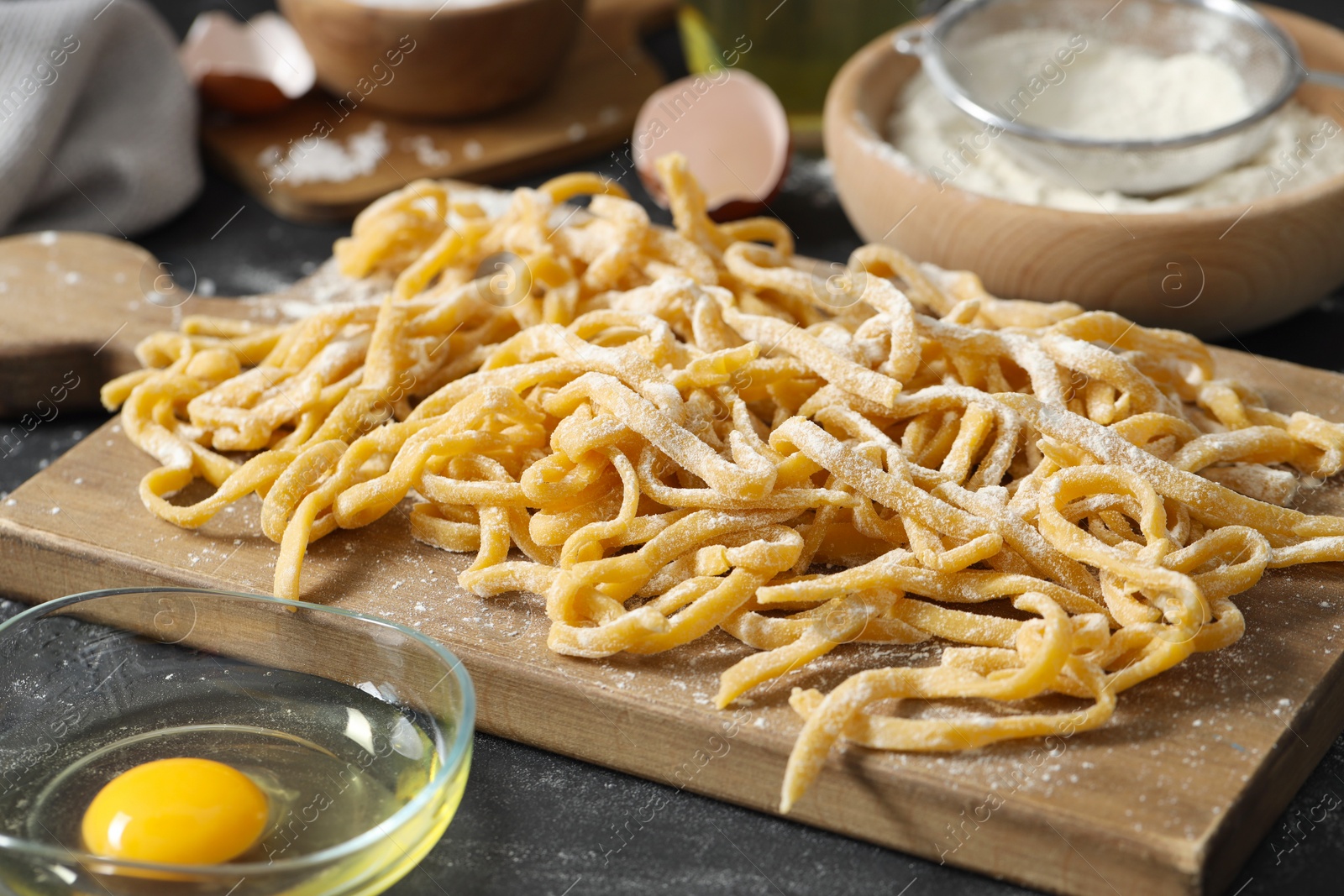 Photo of Board with homemade pasta, flour and ingredients on dark table, closeup