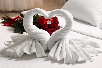 Photo of Honeymoon. Swans made of towels and beautiful red roses on bed in room